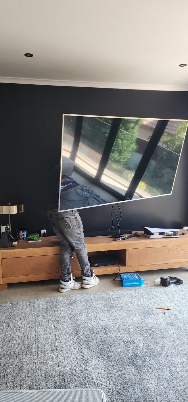 Technician mounting a large flat-screen TV on a living room wall